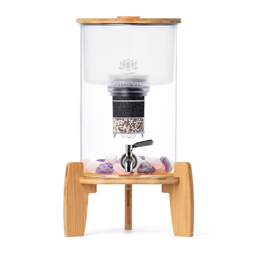 Ein Stand-Wasserfilter aus Glas mit einem Sockel und Deckel aus Bambus, einem Edelstahl-Zapfhahn und Edelsteinen im Behälter.