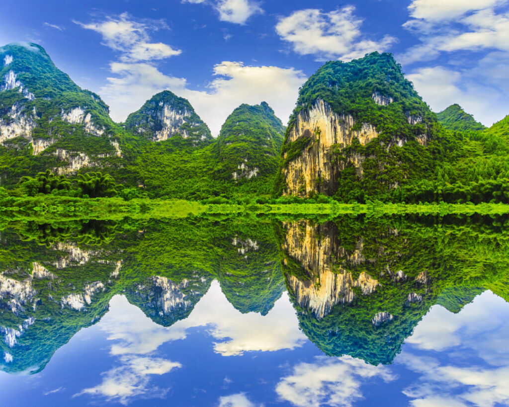 Ruhige Berglandschaft mit üppiger grüner Vegetation, die sich makellos im klaren Wasser eines Sees spiegelt.
