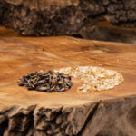 Zwei Haufen mit polierten Kristallsteinen, Tigerauge und Goldener Beryll, liegen auf einer rustikalen Holzscheibe.