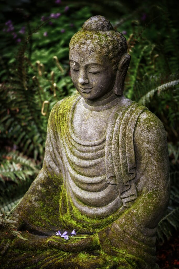 Eine von Moos überwachsene Buddha-Statue in einem Garten, die Ruhe und Naturverbundenheit ausstrahlt.