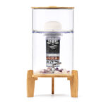 Eleganter Glas-Wasserfilter mit Bambus-Deckel und -Sockel von Lotus Vita, auf einem Bambusgestell stehend. Die Filterkartusche und Edelsteine im Inneren sind sichtbar.