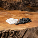 Zwei Haufen mit schwarzen Turmalin- und weißen Milchopal-Edelsteinen auf einer rustikalen Holzoberfläche.